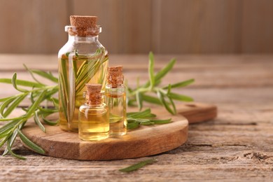 Photo of Aromatic essential oils in bottles and rosemary on wooden table, closeup. Space for text