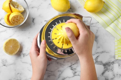 Woman squeezing lemon juice with reamer at white marble table, top view