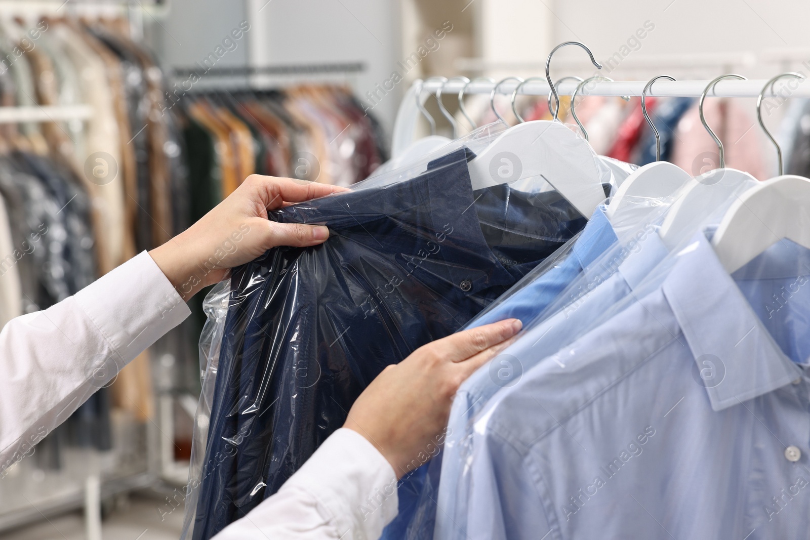 Photo of Dry-cleaning service. Woman taking shirt in plastic bag from rack indoors, closeup