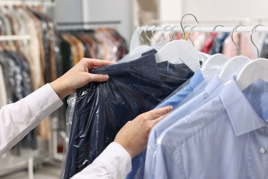 Dry-cleaning service. Woman taking shirt in plastic bag from rack indoors, closeup