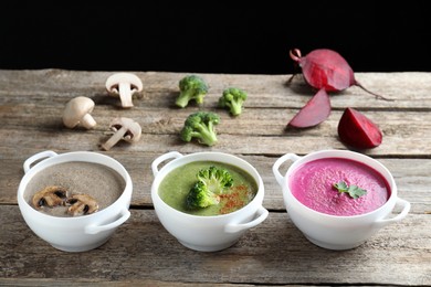 Photo of Different tasty cream soups in bowls and ingredients on old wooden table