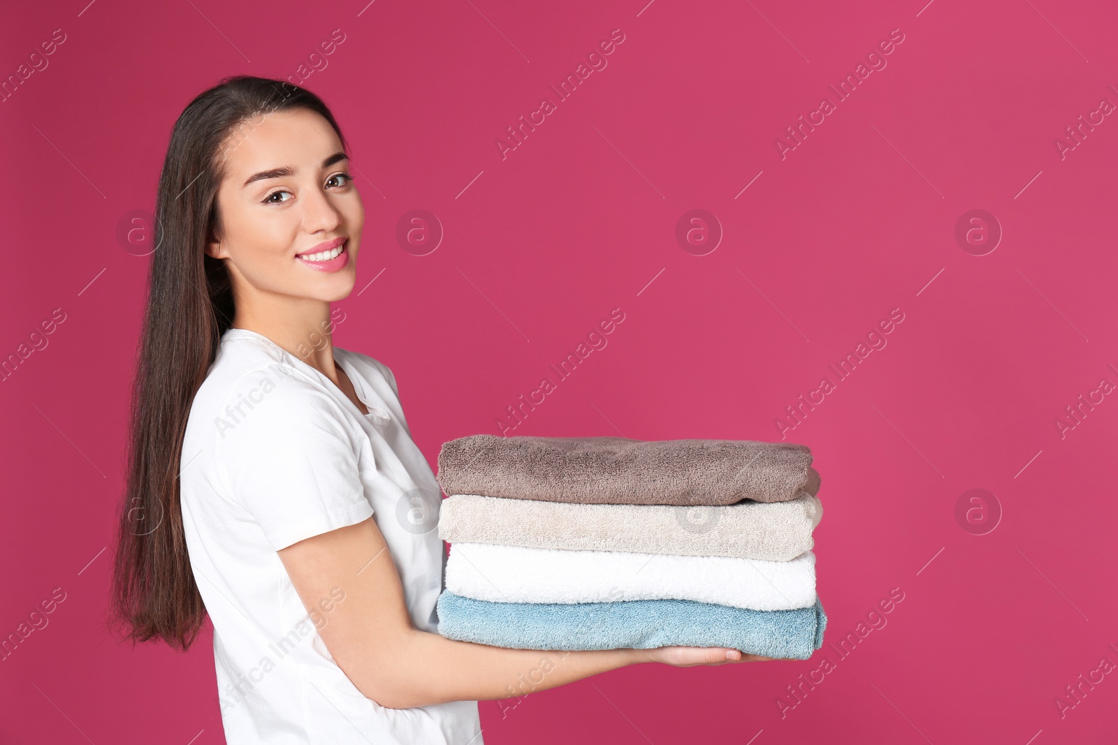 Photo of Happy young woman holding clean towels on color background, space for text. Laundry day