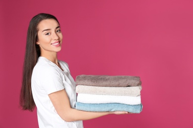 Happy young woman holding clean towels on color background, space for text. Laundry day