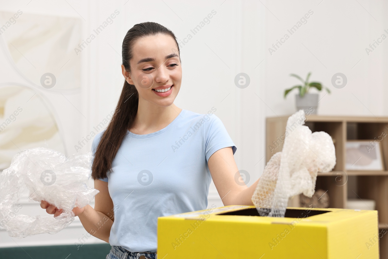 Photo of Garbage sorting. Smiling woman throwing plastic package into cardboard box in room