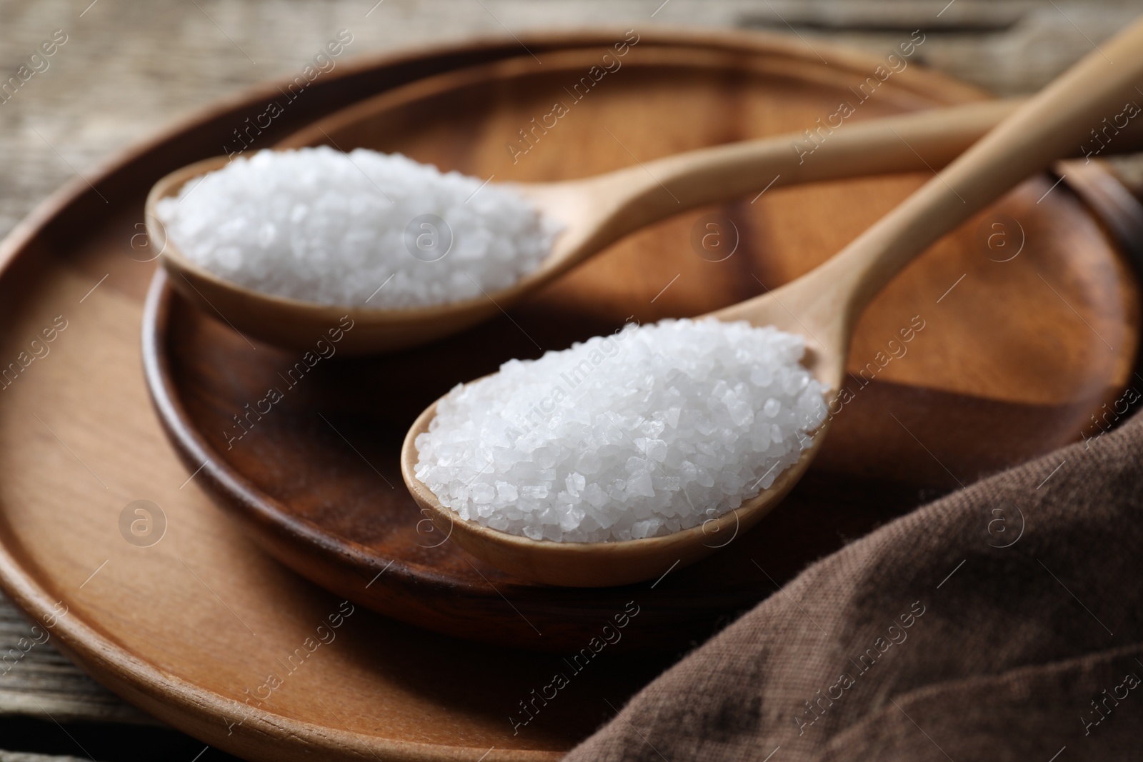 Photo of Organic salt in spoons on wooden table, closeup