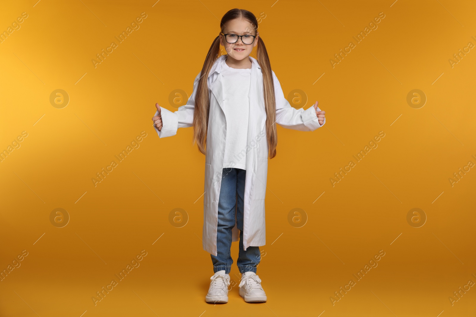 Photo of Little girl in medical uniform showing thumbs up on yellow background