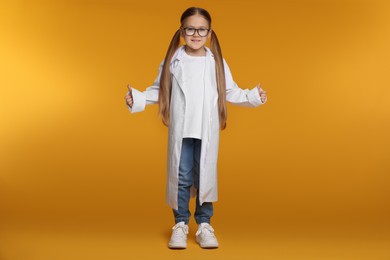 Photo of Little girl in medical uniform showing thumbs up on yellow background