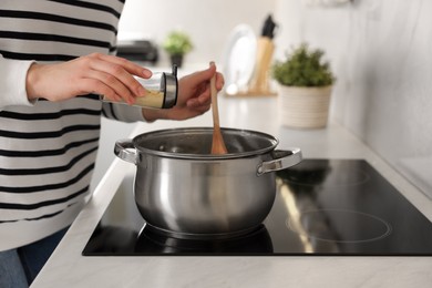 Woman adding spices into pot with soup in kitchen, closeup