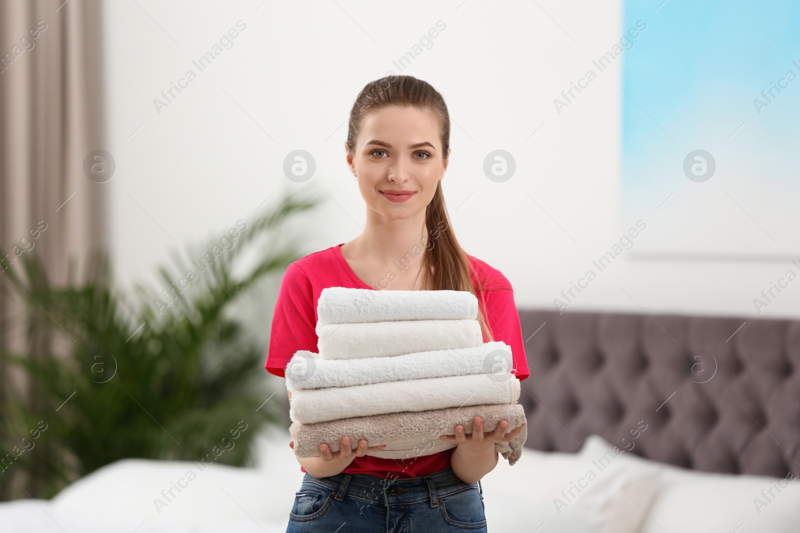 Photo of Woman holding folded clean towels in bedroom. Laundry day