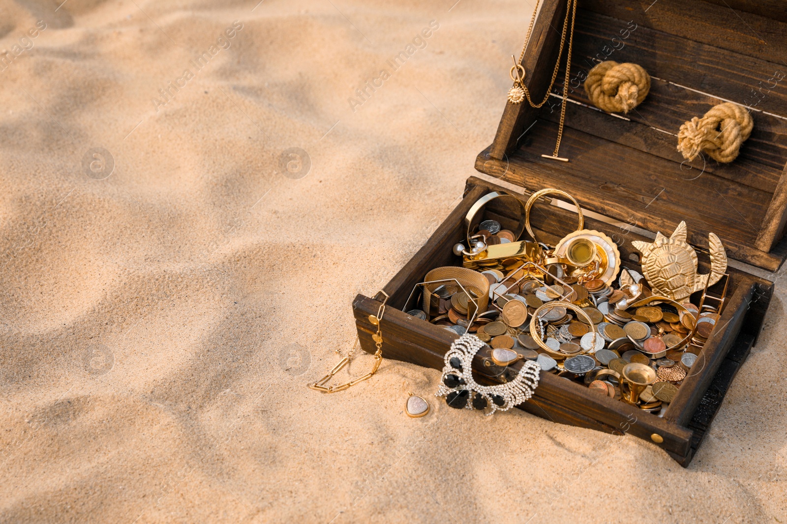 Photo of Open wooden treasure chest on sand, space for text