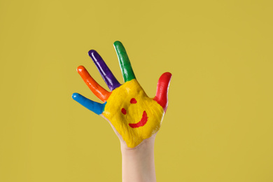 Photo of Kid with smiling face drawn on palm against yellow background, closeup