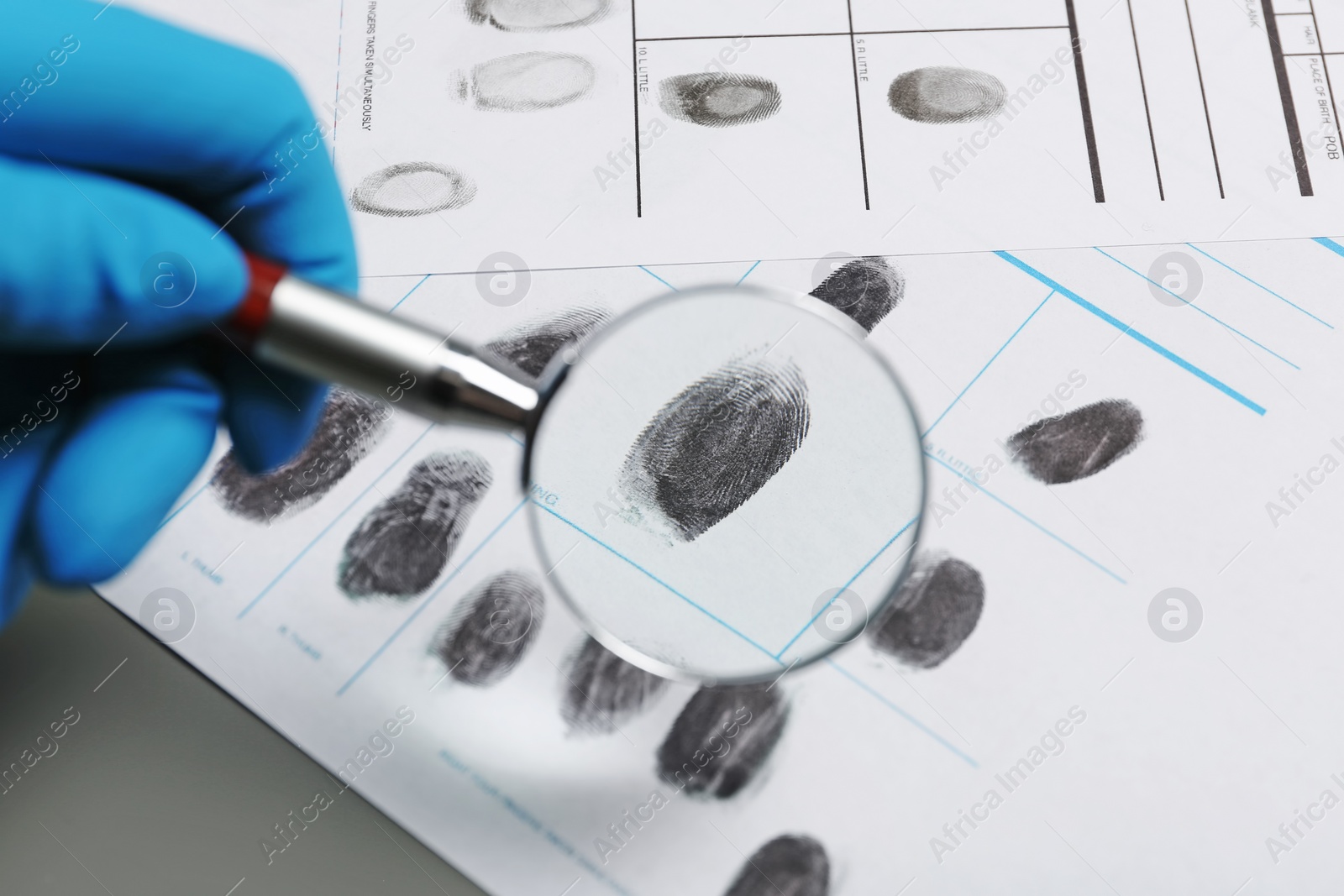 Photo of Criminalist exploring fingerprints with magnifying glass, closeup