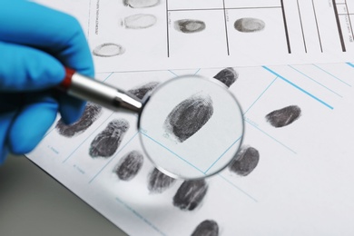 Photo of Criminalist exploring fingerprints with magnifying glass, closeup