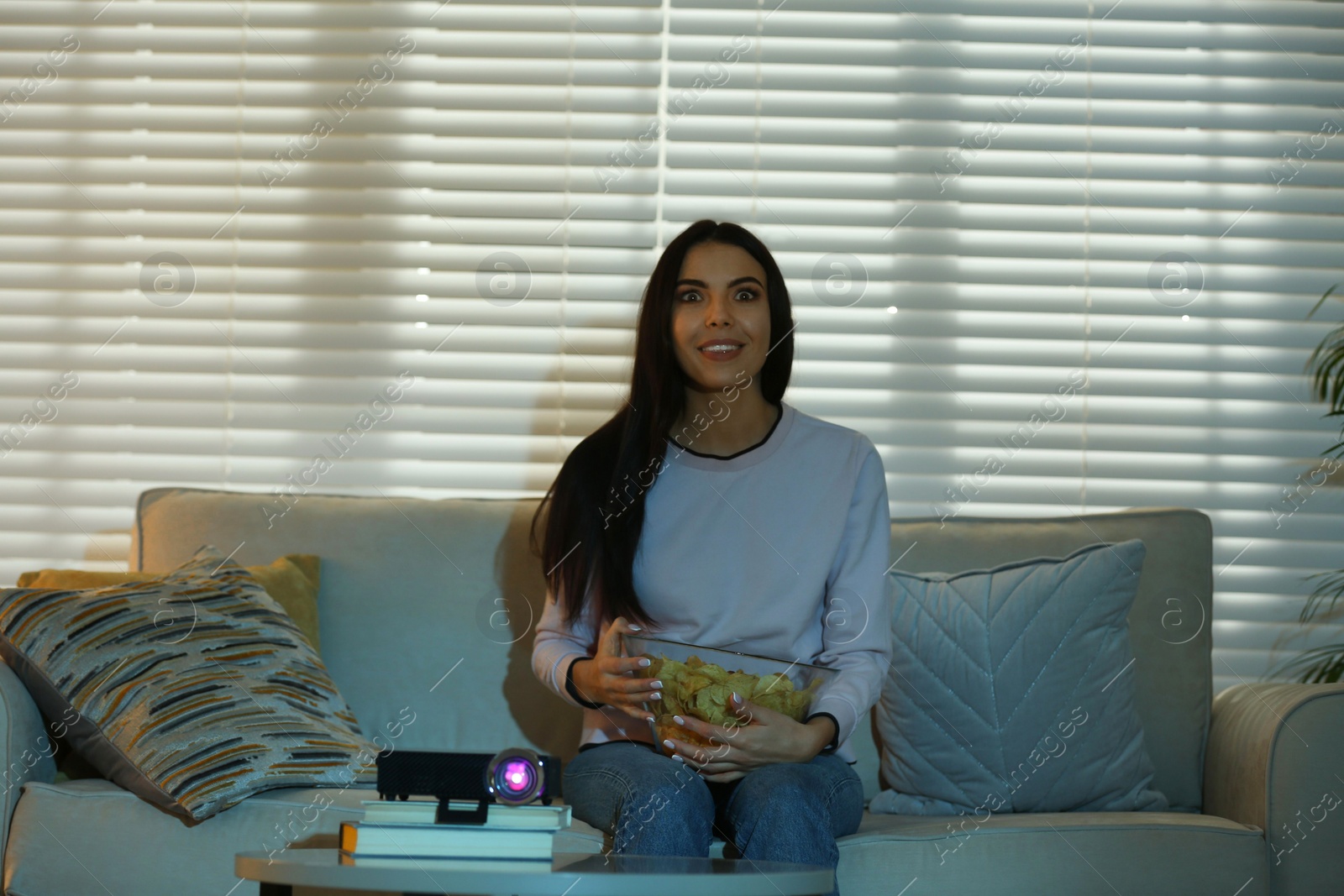 Photo of Young woman watching movie using video projector at home