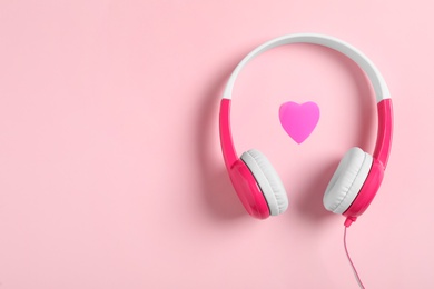 Photo of Modern headphones and heart on pink background, flat lay with space for text. Listening love music songs