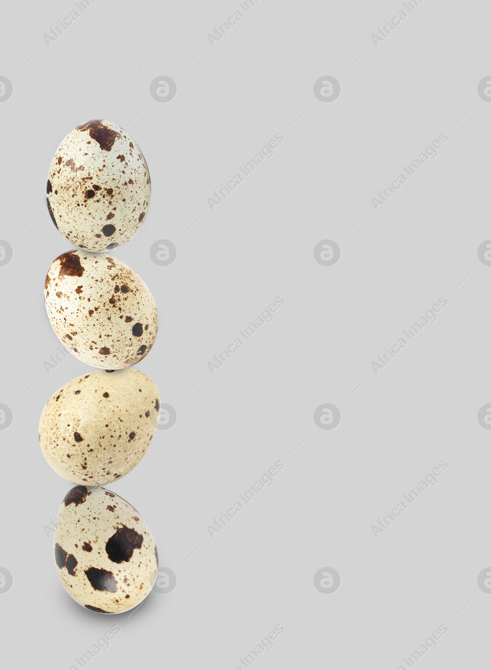 Image of Stacked speckled quail eggs on light grey background. Space for text