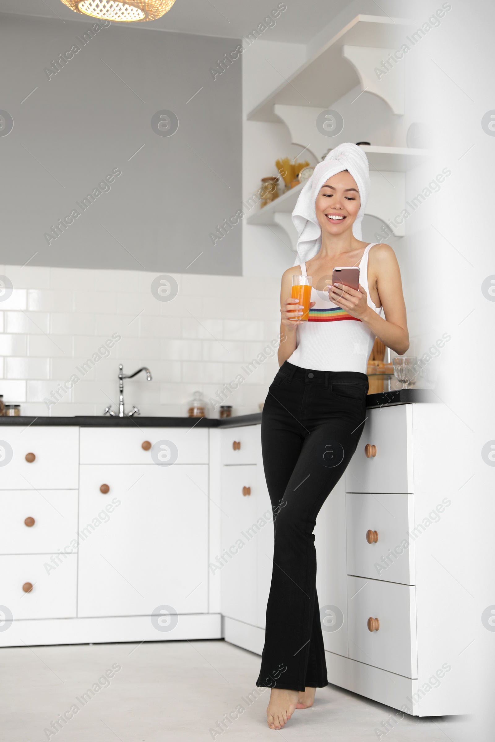 Photo of Beautiful young woman with towel, phone and glass of juice in kitchen