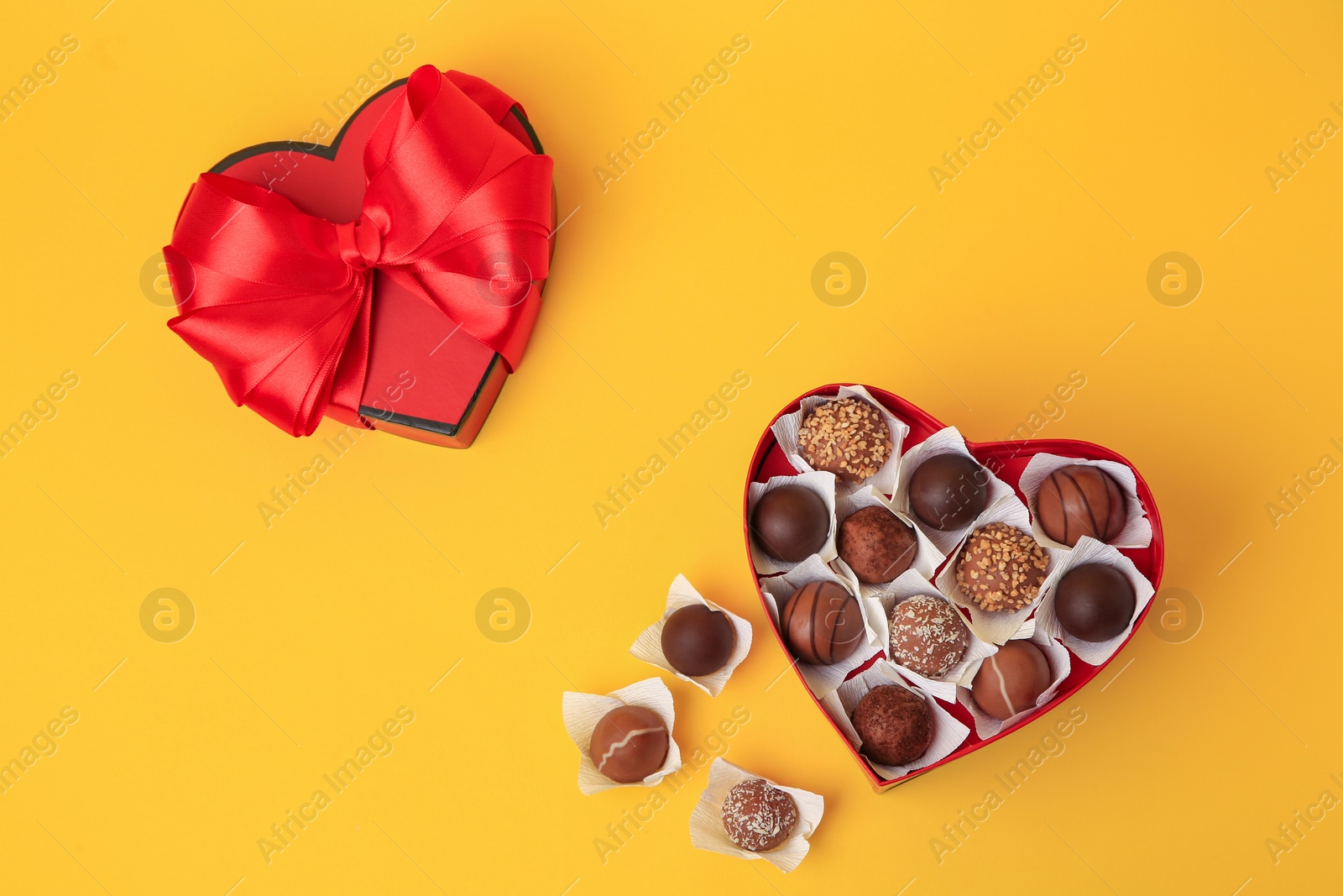 Photo of Heart shaped box with delicious chocolate candies on yellow background, flat lay