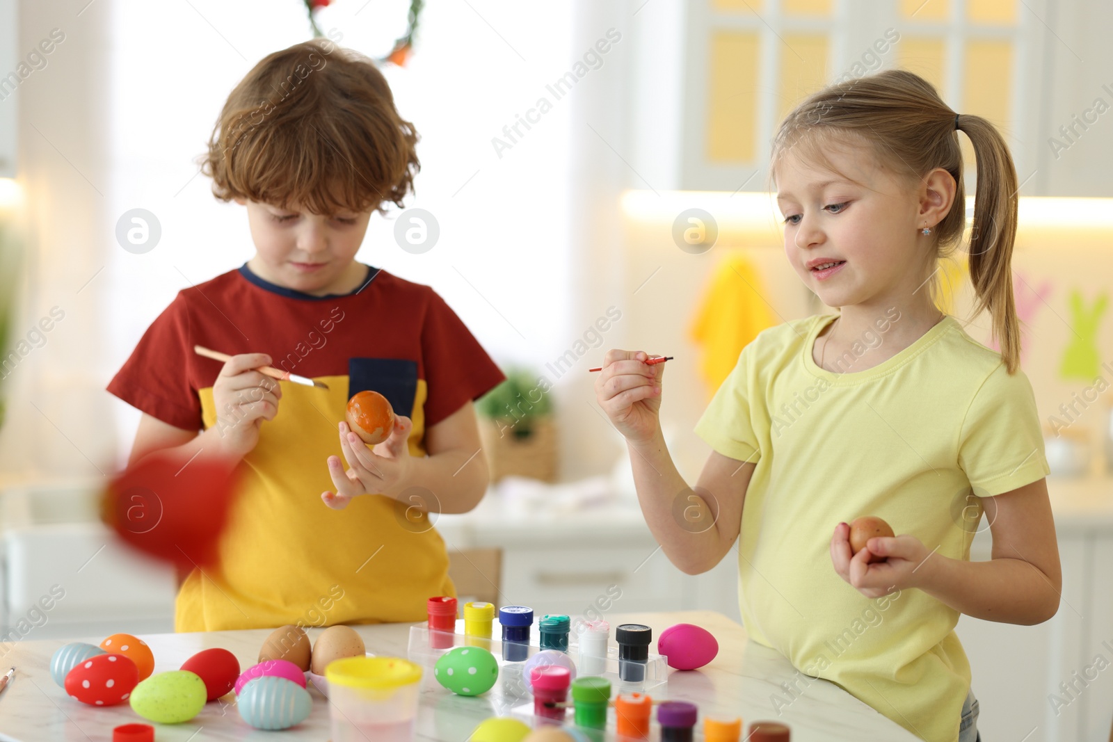 Photo of Easter celebration. Cute children painting eggs at white table in kitchen