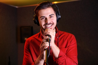 Young singer with microphone recording song in studio