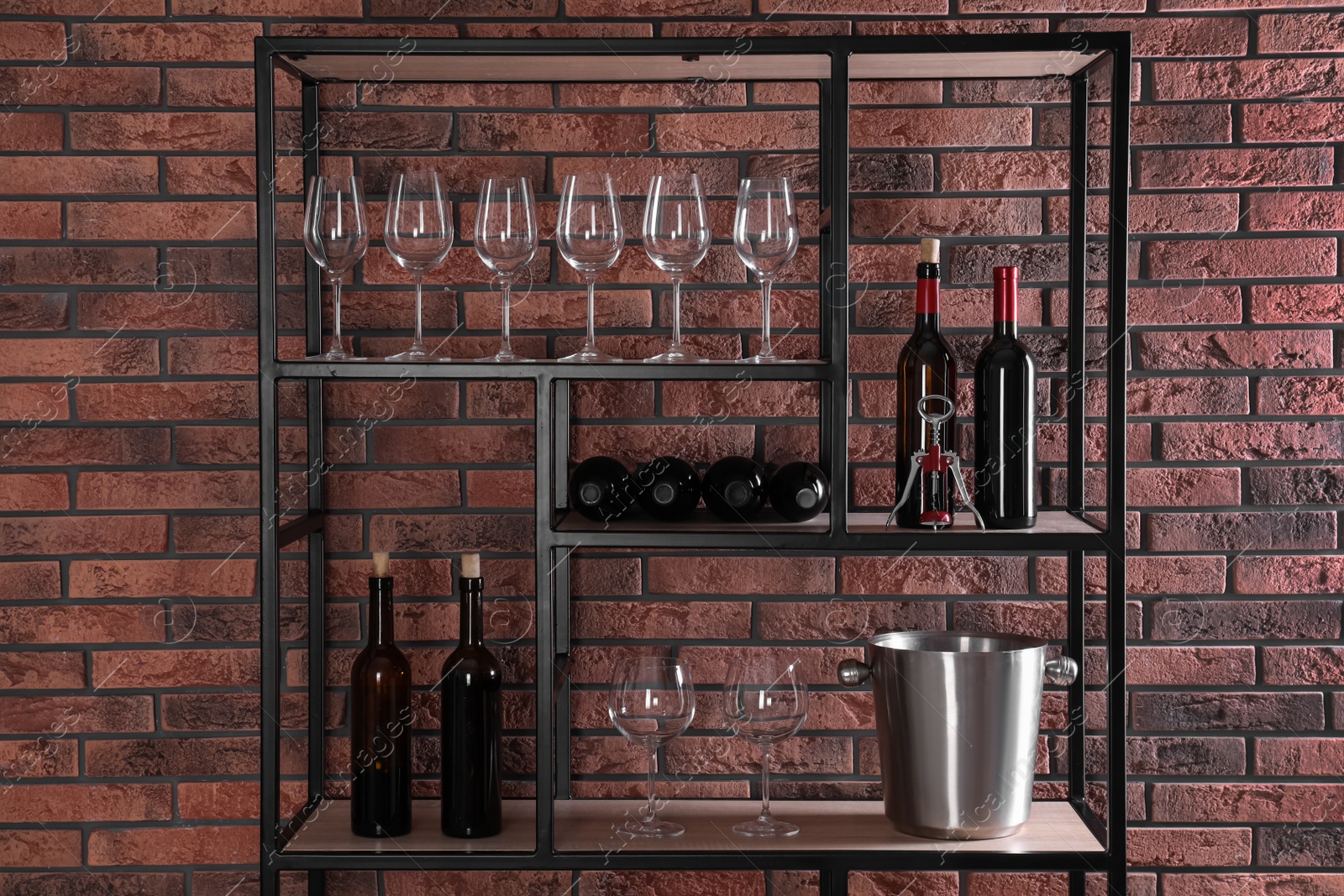 Photo of Rack with bottles of wine and glasses near brick wall