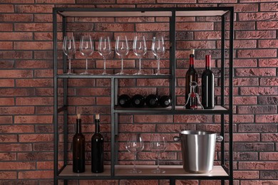 Photo of Rack with bottles of wine and glasses near brick wall