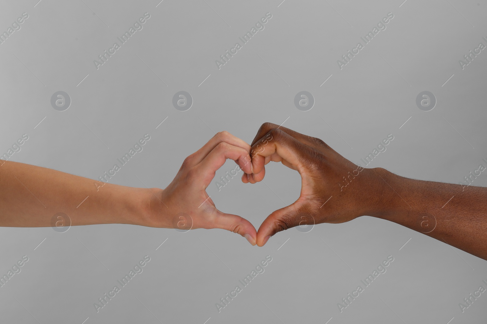 Photo of Woman and African American man making heart with hands on light grey background, closeup