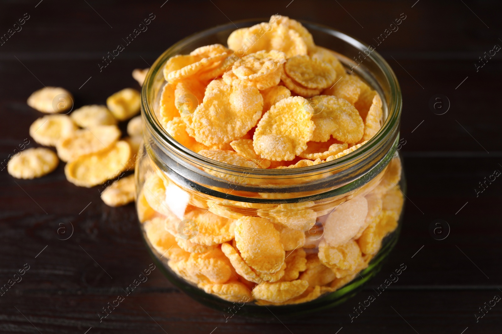 Photo of Jar of tasty crispy corn flakes on wooden table, closeup