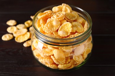 Photo of Jar of tasty crispy corn flakes on wooden table, closeup