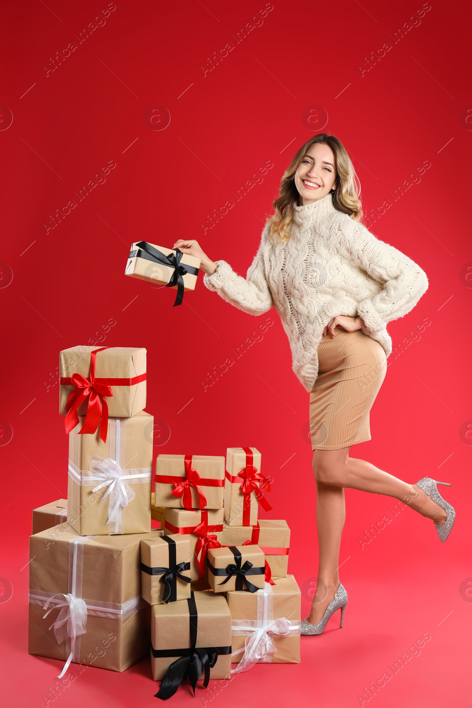 Photo of Beautiful young woman with pile of Christmas presents on red background