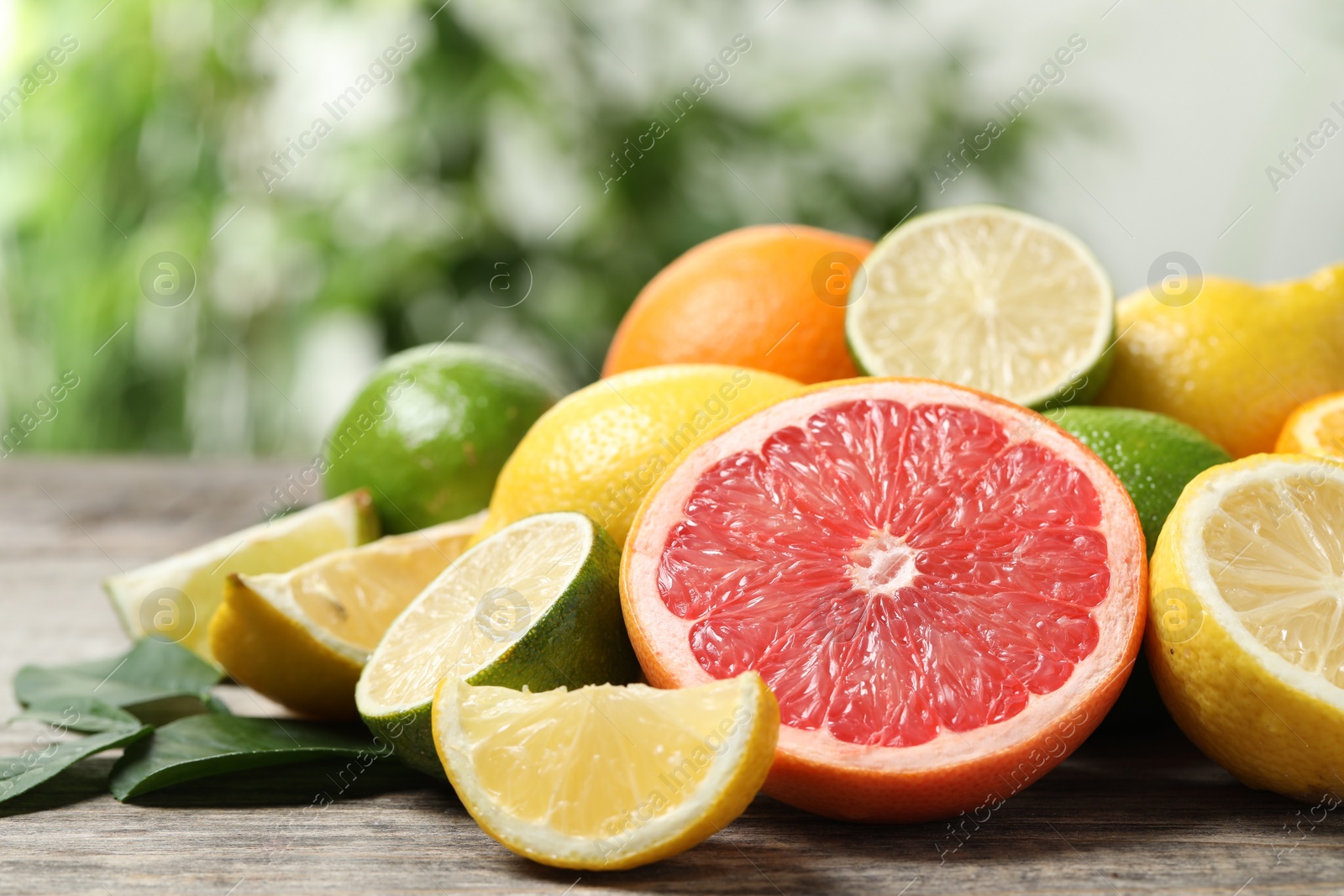 Photo of Different fresh citrus fruits and leaves on wooden table against blurred background, closeup