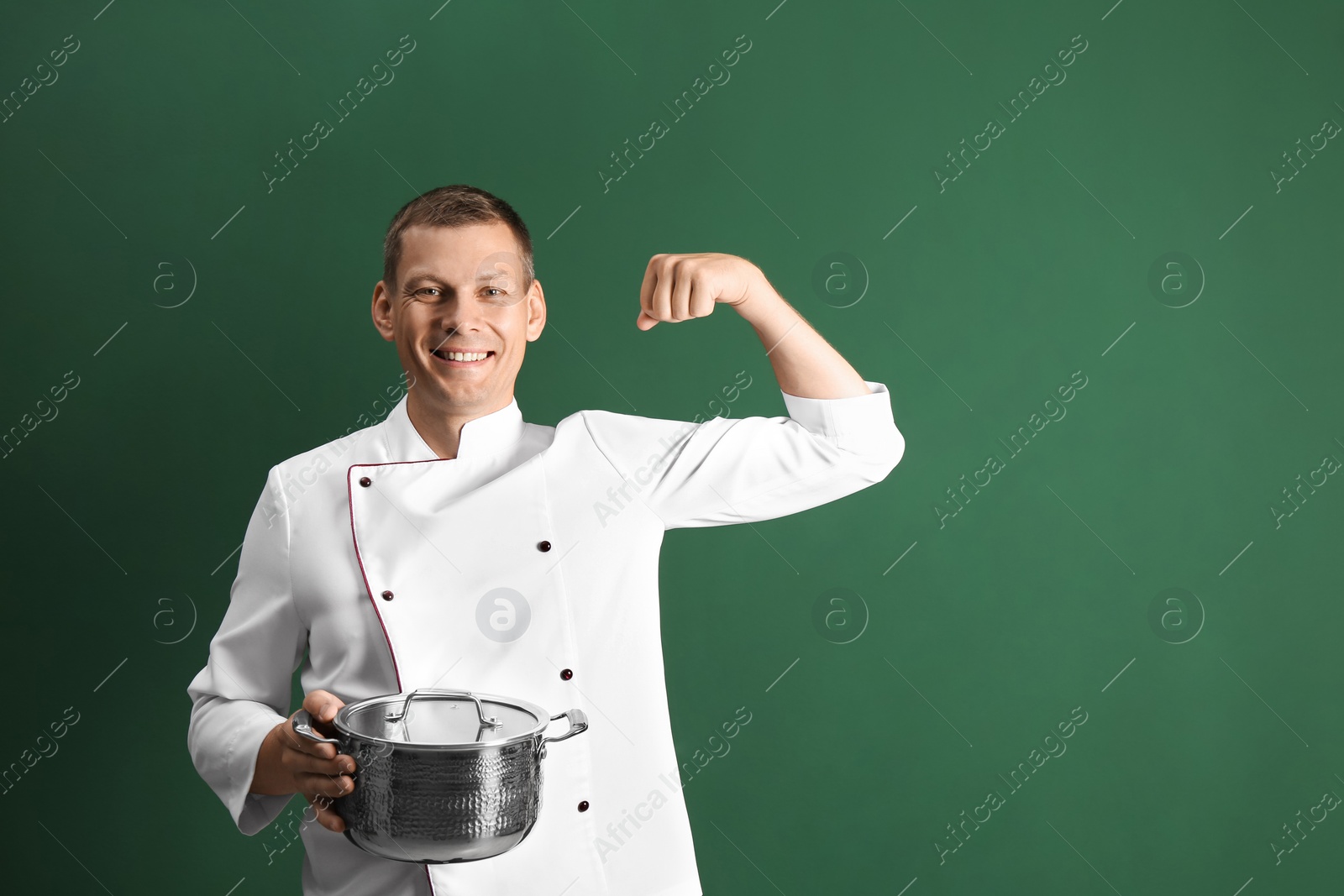 Photo of Happy male chef with cooking pot on dark green background. Space for text