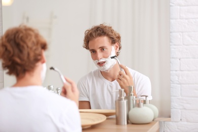 Photo of Young handsome man shaving in bathroom