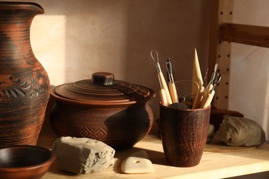 Photo of Set of different crafting tools and clay dishes on wooden rack in workshop