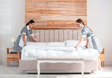 Photo of Young chambermaids making bed in hotel room