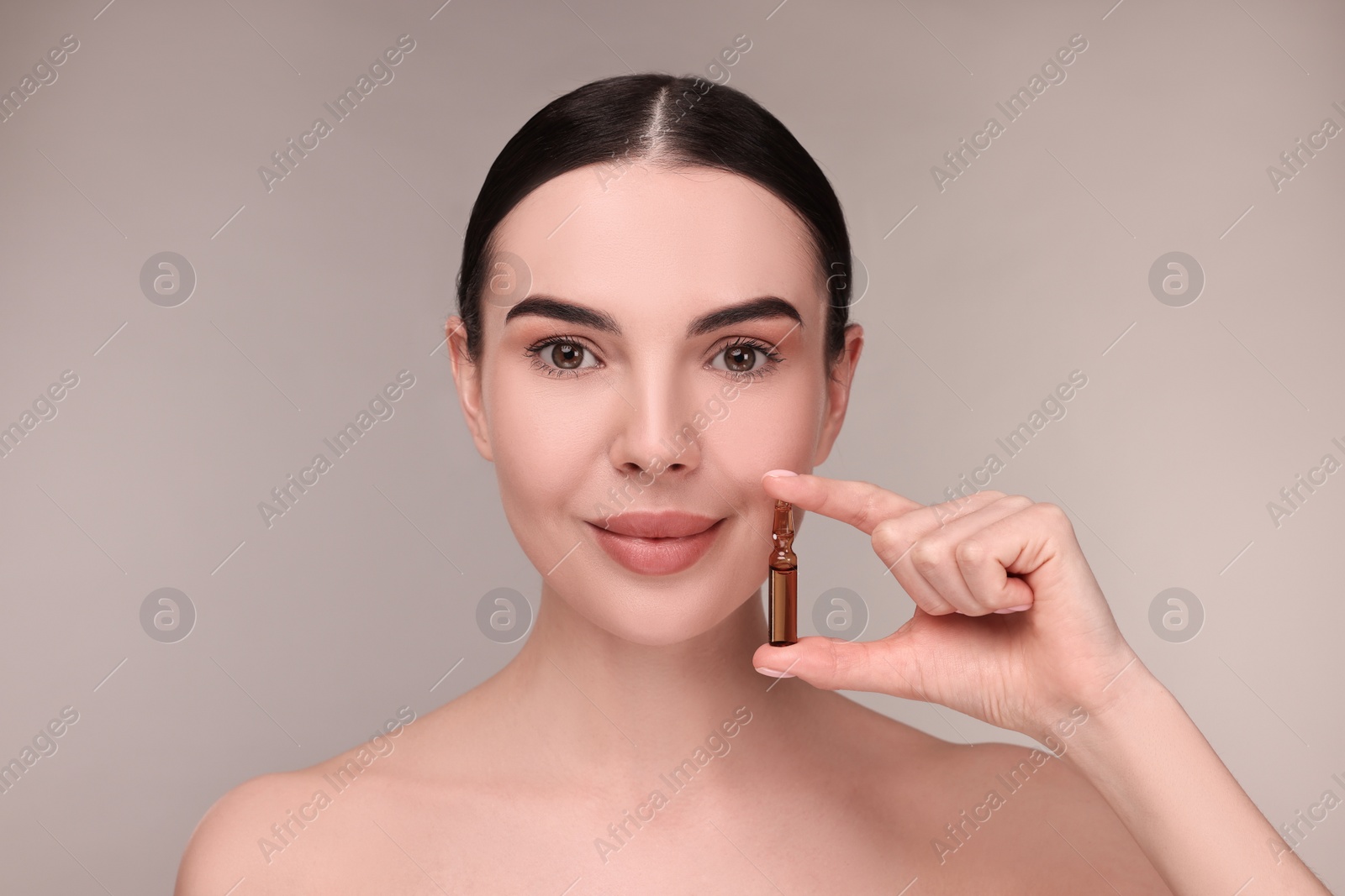 Photo of Beautiful young woman holding skincare ampoule on grey background