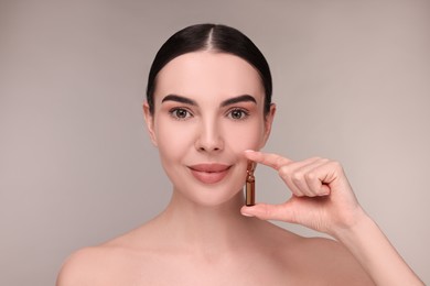 Beautiful young woman holding skincare ampoule on grey background