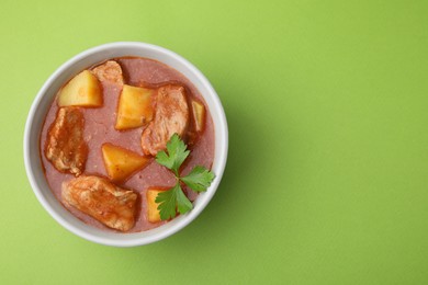 Delicious goulash in bowl on green background, top view. Space for text