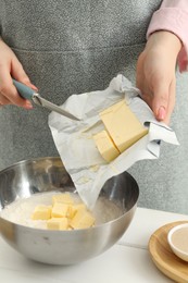 Photo of Woman adding fresh butter into bowl with flour at white wooden table, closeup