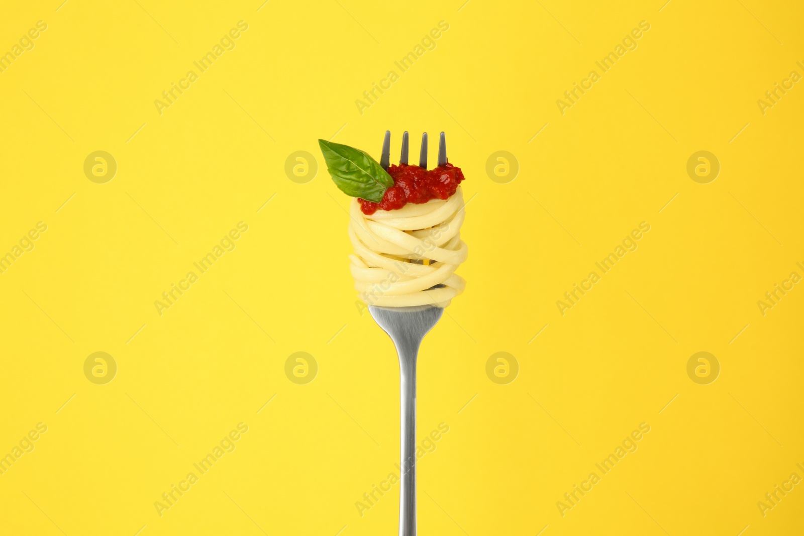 Photo of Fork with tasty pasta, tomato sauce and basil on yellow background