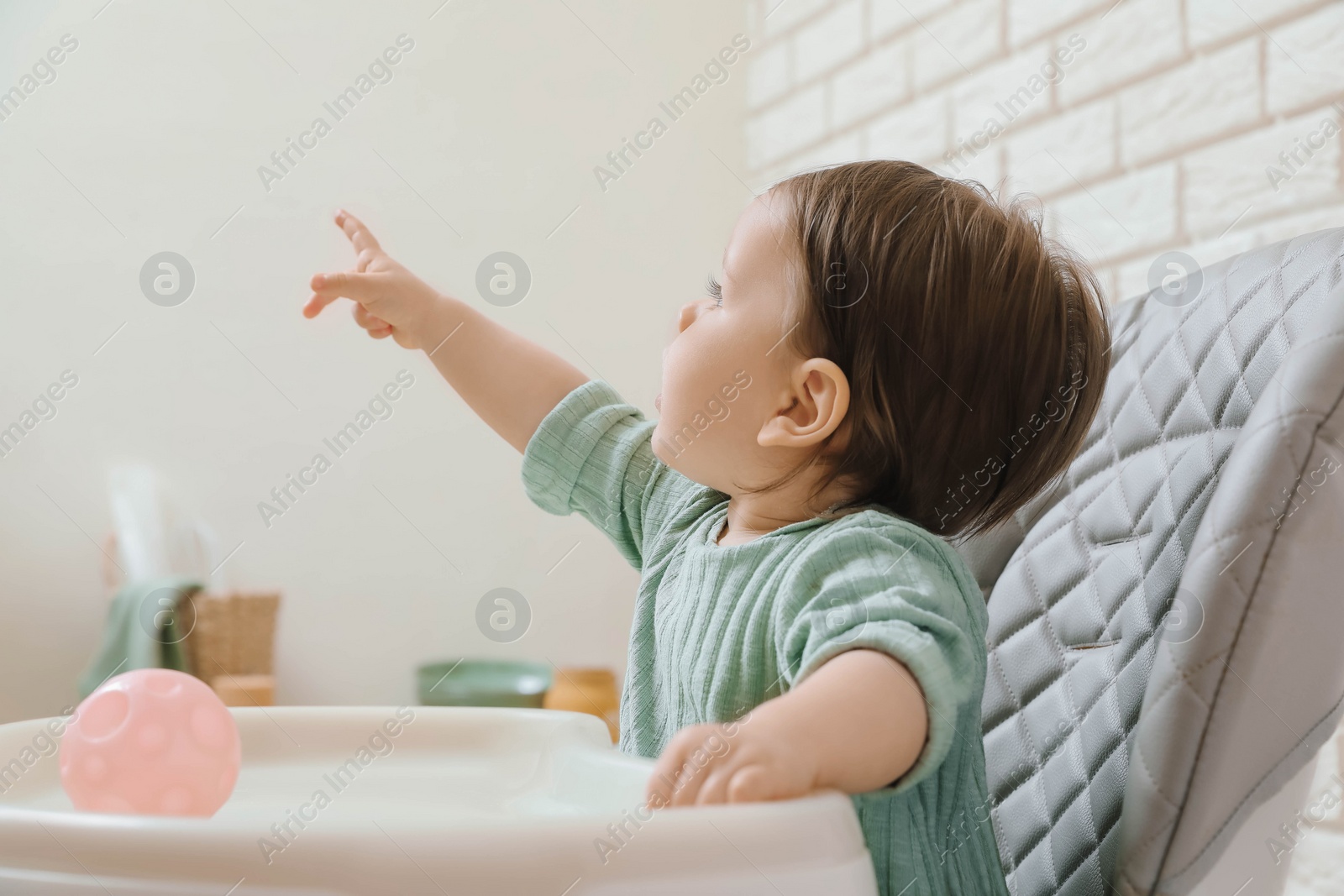 Photo of Cute little baby pointing at something in high chair indoors
