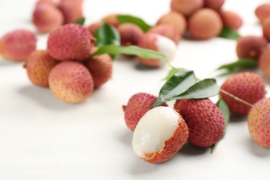 Photo of Fresh ripe lychees with leaves on white wooden table, closeup. Space for text