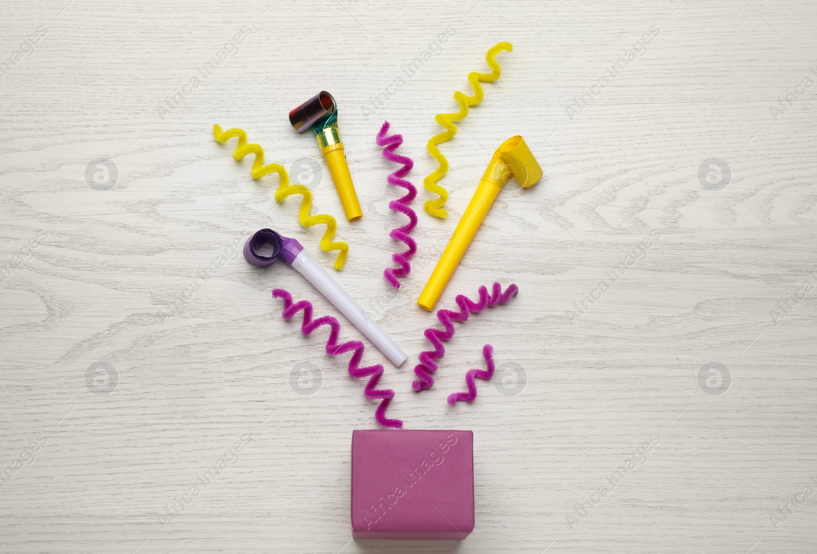 Photo of Party horns, streamers and box on white wooden table, flat lay