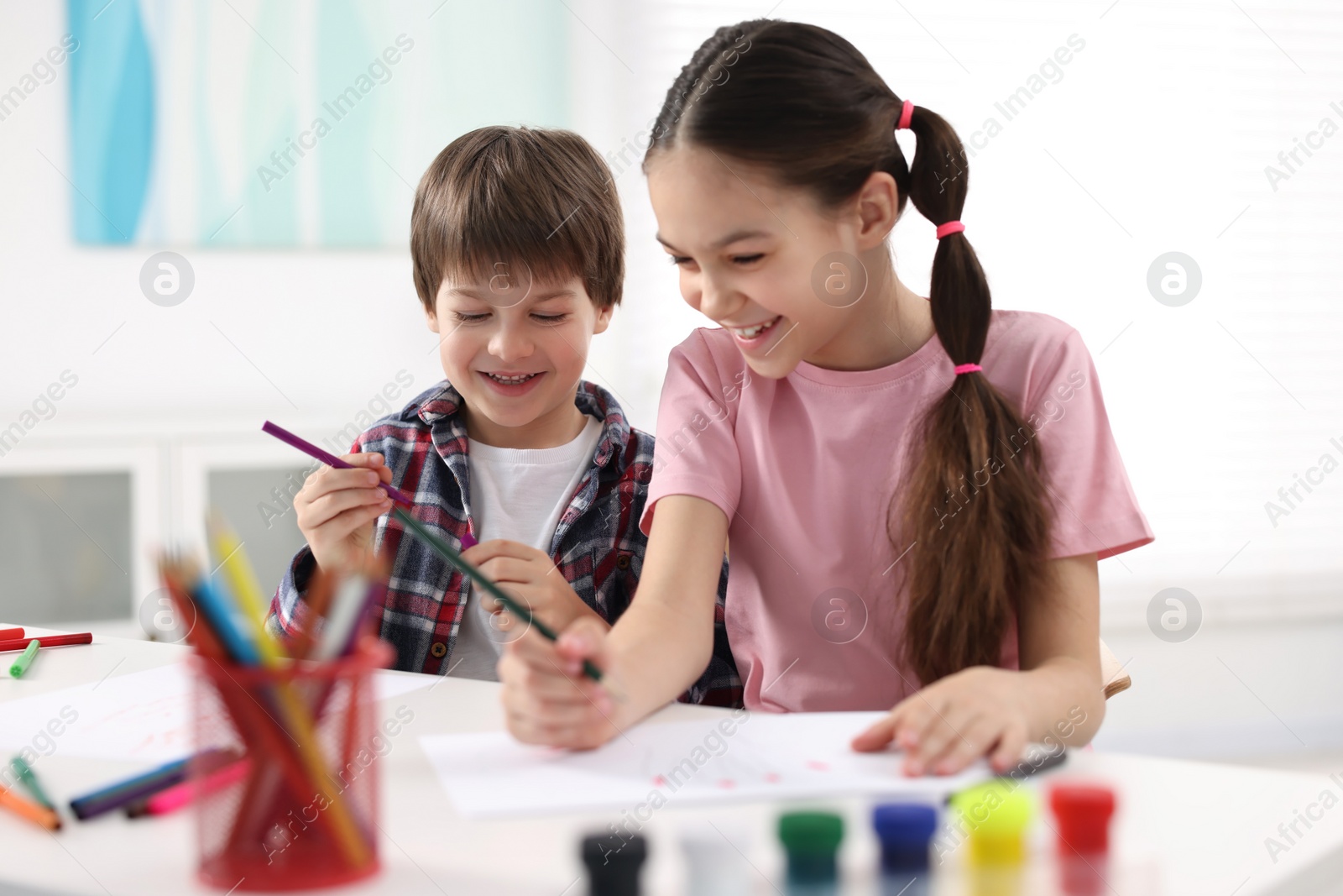 Photo of Happy brother and sister drawing at white table in room