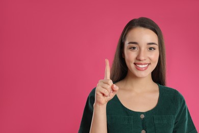 Photo of Woman showing number one with her hand on pink background. Space for text