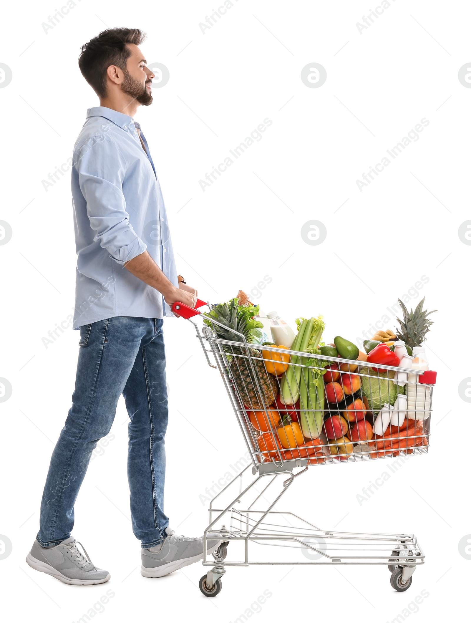 Photo of Young man with shopping cart full of groceries on white background