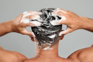 Photo of Man washing hair on grey background, back view