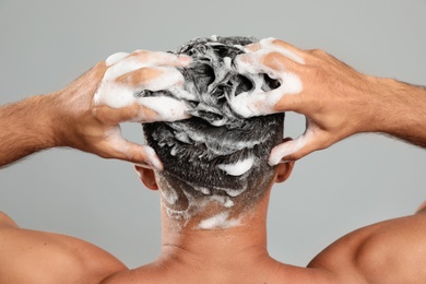 Man washing hair on grey background, back view