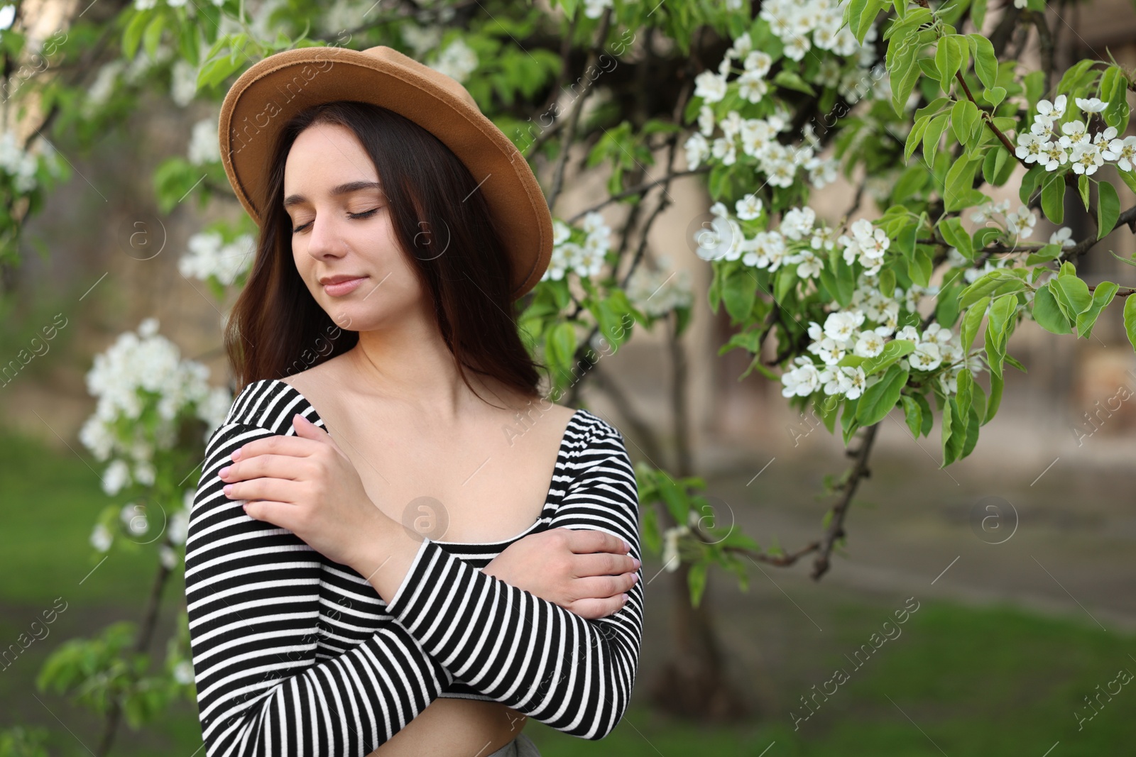 Photo of Beautiful woman in hat near blossoming tree on spring day