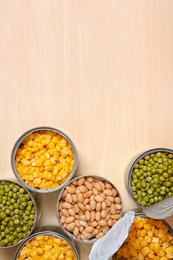 Photo of Open tin cans of conserved vegetables on wooden table, flat lay with space for text